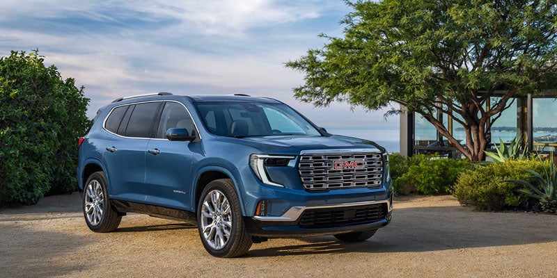 A blue 2026 GMC Acadia standing natural greenery.