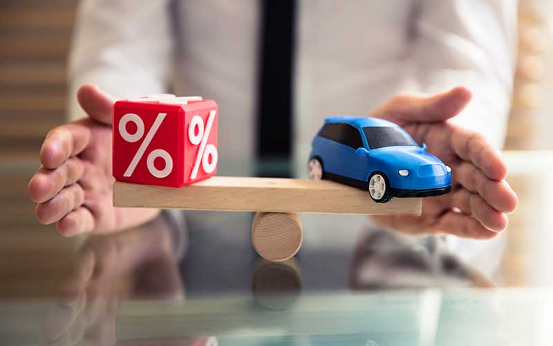 A toy car and red cube with percent sign on wood which holds by a person